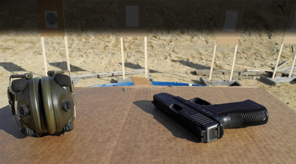 Pistol, magazines and hearing protection laid out on a range bench